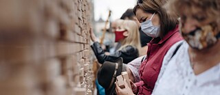 Besucherinnen und Besucher ziehen Holzklötzchen, auf die Zitate gedruckt sind, aus der Wand.