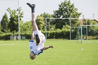 Chlapec na fotbalovém hřišti skočí salto.