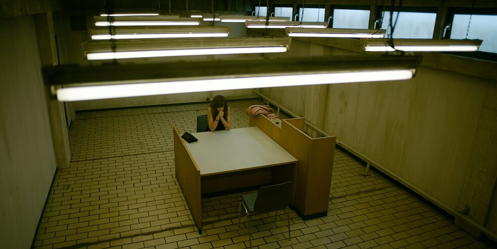 "Perfume - Bondage": View from above into the police interrogation room. Elena Seliger (Natalia Belitski) is sitting at a table.