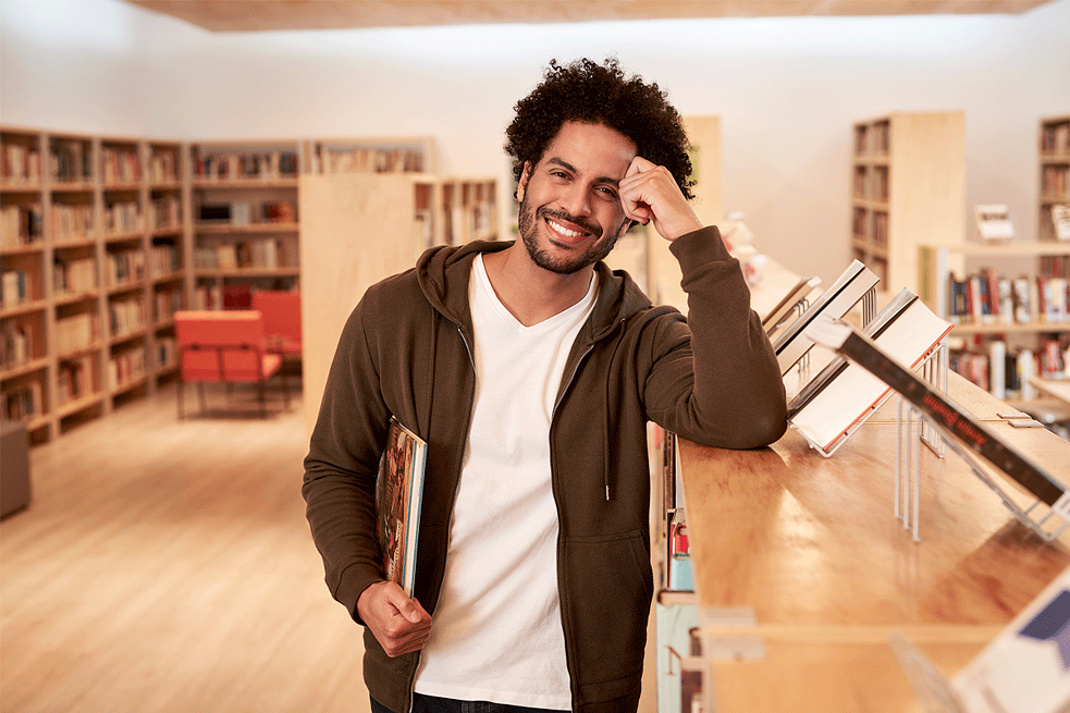 junger mann in der bibliothek schaut in die kamera und lächelt