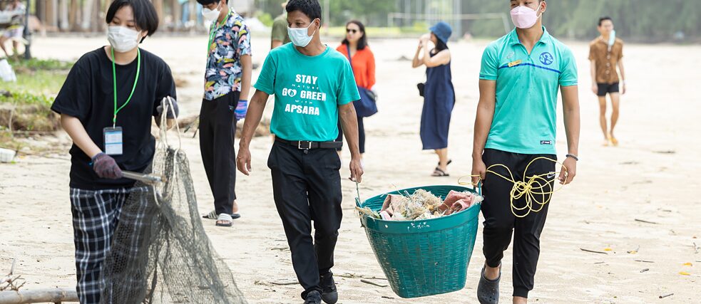 Menschen heben Müll vom Strand auf und sammeln ihn in großen Körben.