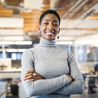 A young, confident woman in a grey sweater looks at the camera and smiles