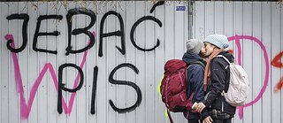Photo is showing two young people kissing near dirty politically oriented graffiti. 