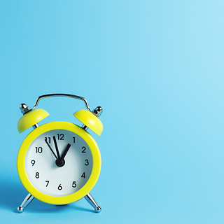 a yellow alarmclock in front of a light-blue background