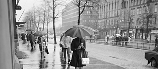 Mustavalko kuva naisesta sateenvarjon kanssa Helsingin kadulla.