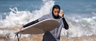Eine junge Frau mit Surfbrett kommt aus dem Meer