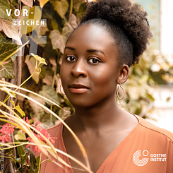 A portrait of a young Black woman standing in front of a hedge with green leaves and pink flowers. In the top left corner is a semi-transparent hashtag sign and above it the word Vorzeichen in white. In the bottom right corner is the logo of the Goethe-Institut. 