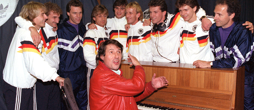 Nazionale di calcio maschile tedesca in uno studio di registrazione, attorno a un pianoforte, con il cantante pop Udo Jürgens seduto al piano.
