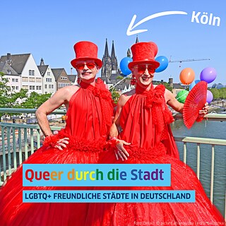 Zwei Personen in roten Kleidern und rotem Hut glücklich in die Kamera blickend vor dem Hintergrund des Kölner Stadtpanoramas. 