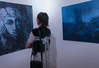 Eine junge Frau steht vor einem Gemälde und betrachtet es.