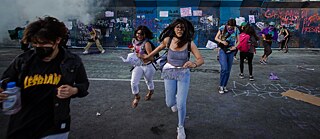 Photo is showing mexican women running in smoke during a protest. 
