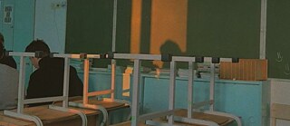 Photo is showing a high school classroom in the setting sun with chairs up. 