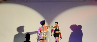 Zwei Tänzerinnen, die auf der Bühne auftreten und deren Schatten auf die Wand hinter ihnen geworfen werden.