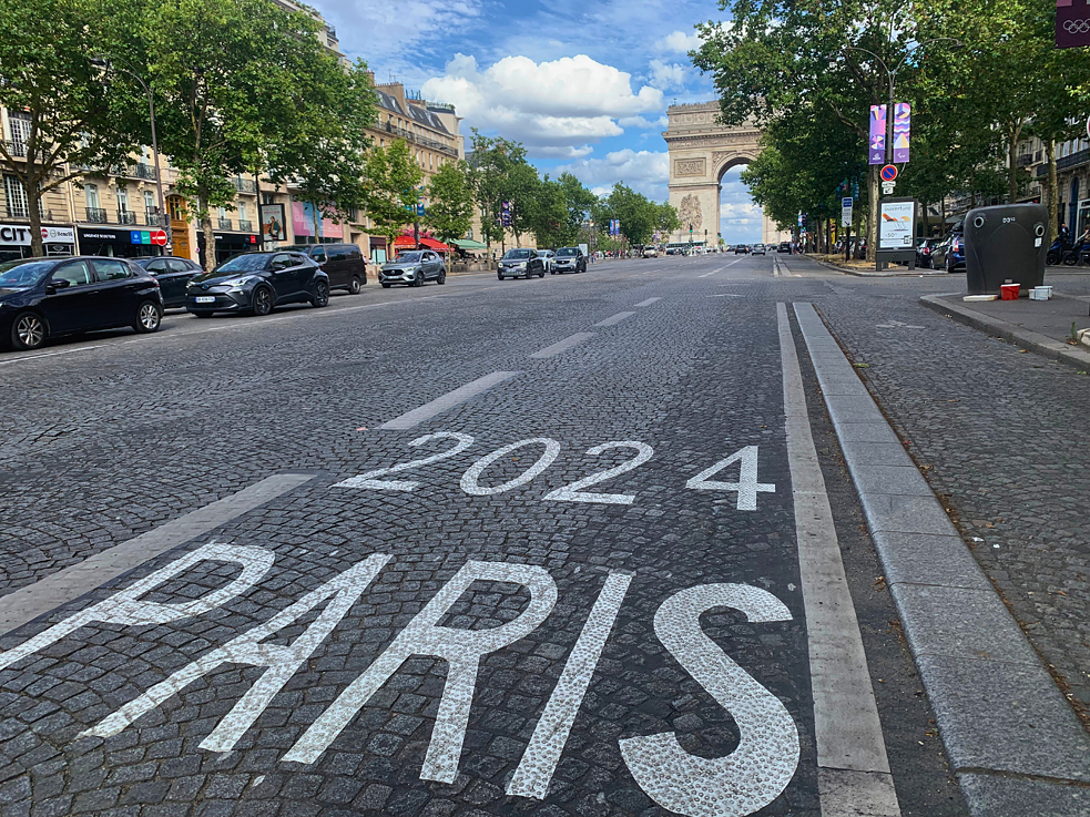 Eine Straße, auf der "Paris 2024" steht. Im Hintergrund der Triumphbogen in Paris.
