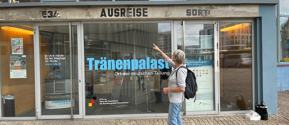 Uta Krebs in front of the Border Crossing  "Tränenpalast" (Palace of Tears), pointing at a sign.