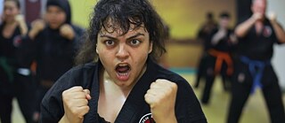 A woman during karate-training. She is wearing a karate suit and holds her hands in fists and screams.